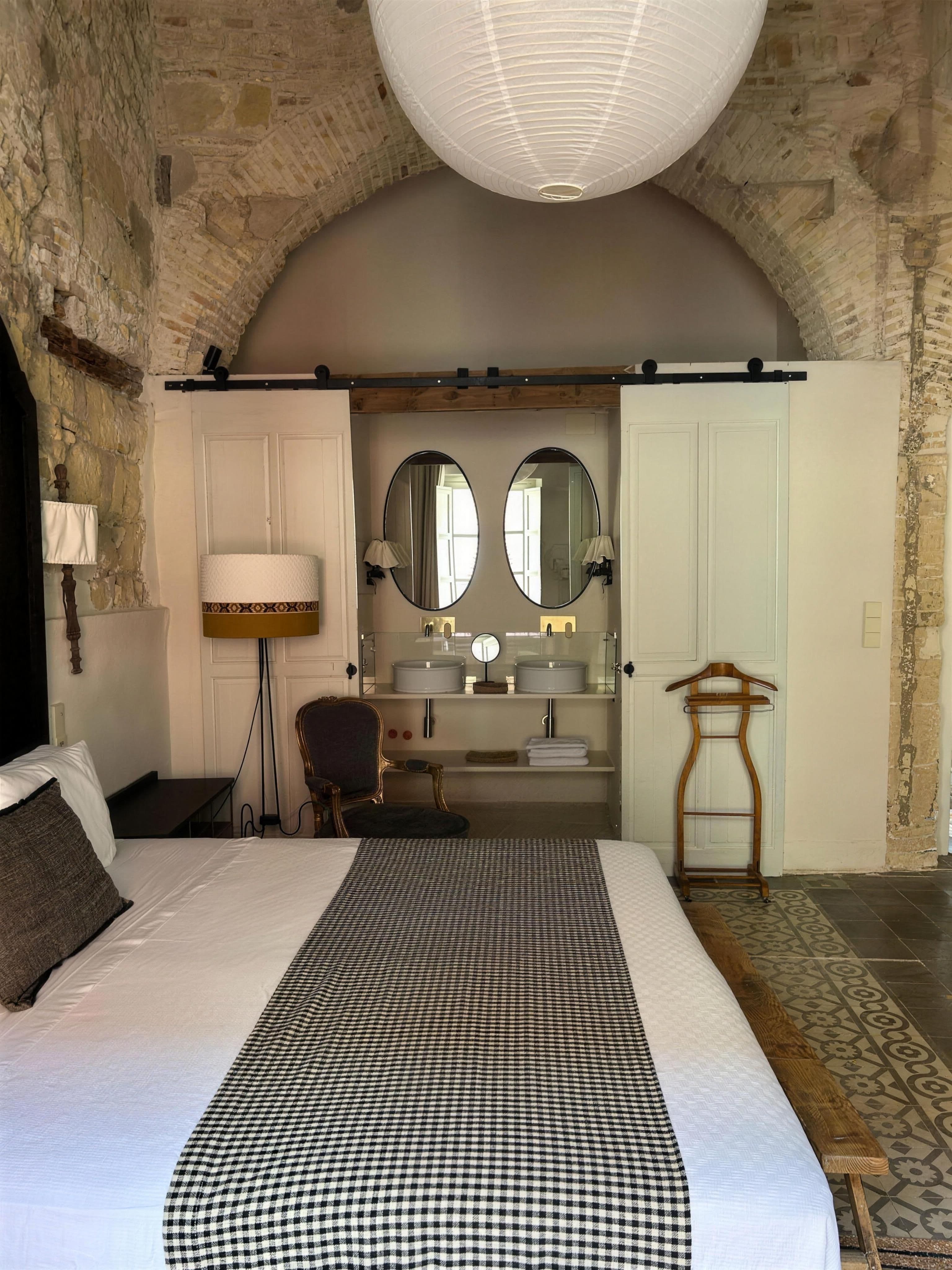 Dormitorio bajo arco de piedra con ropa de cama en cuadros vichy y espejos al fondo