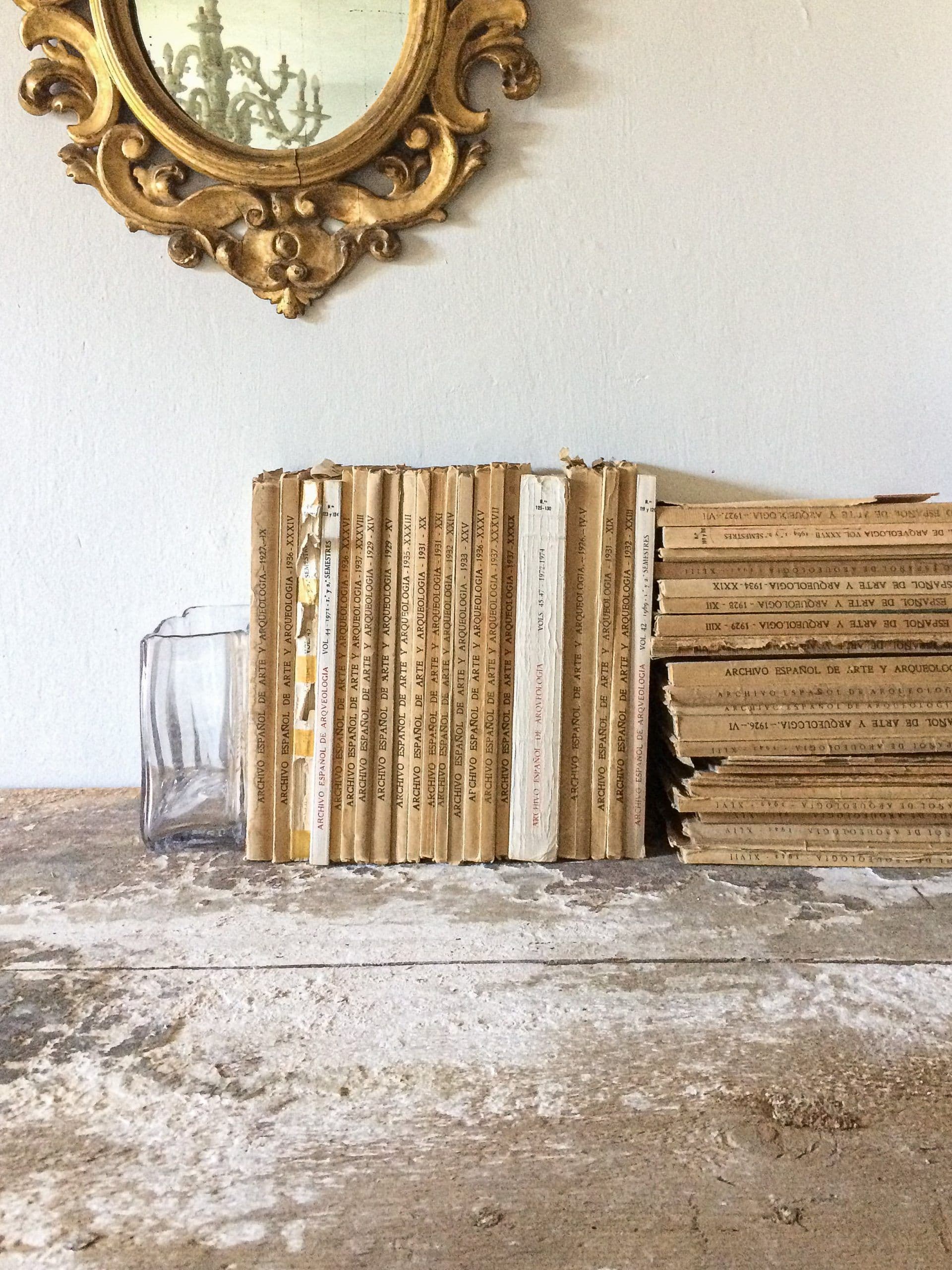 Lomos de libros antiguos dorados sobre repisa de piedra, bajo espejo barroco