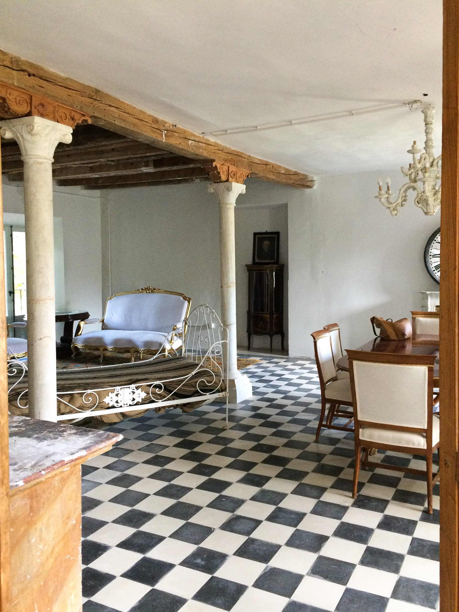 Gran sala de columnas de piedra con suelo damero, cama de hierro de día y sillas tapizadas