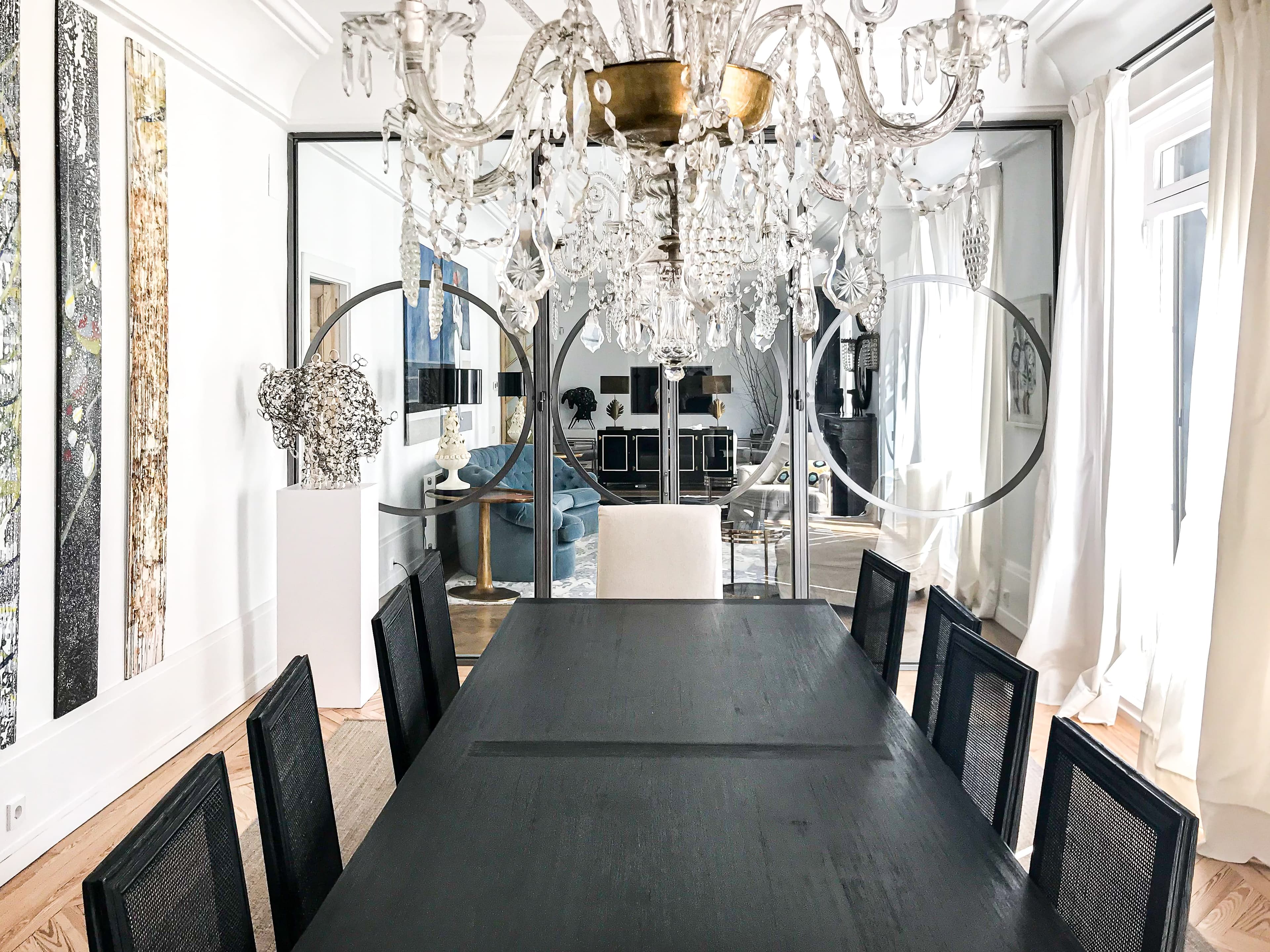 Comedor de mesa negra y pared de espejos envejecidos bajo lámpara de cristal