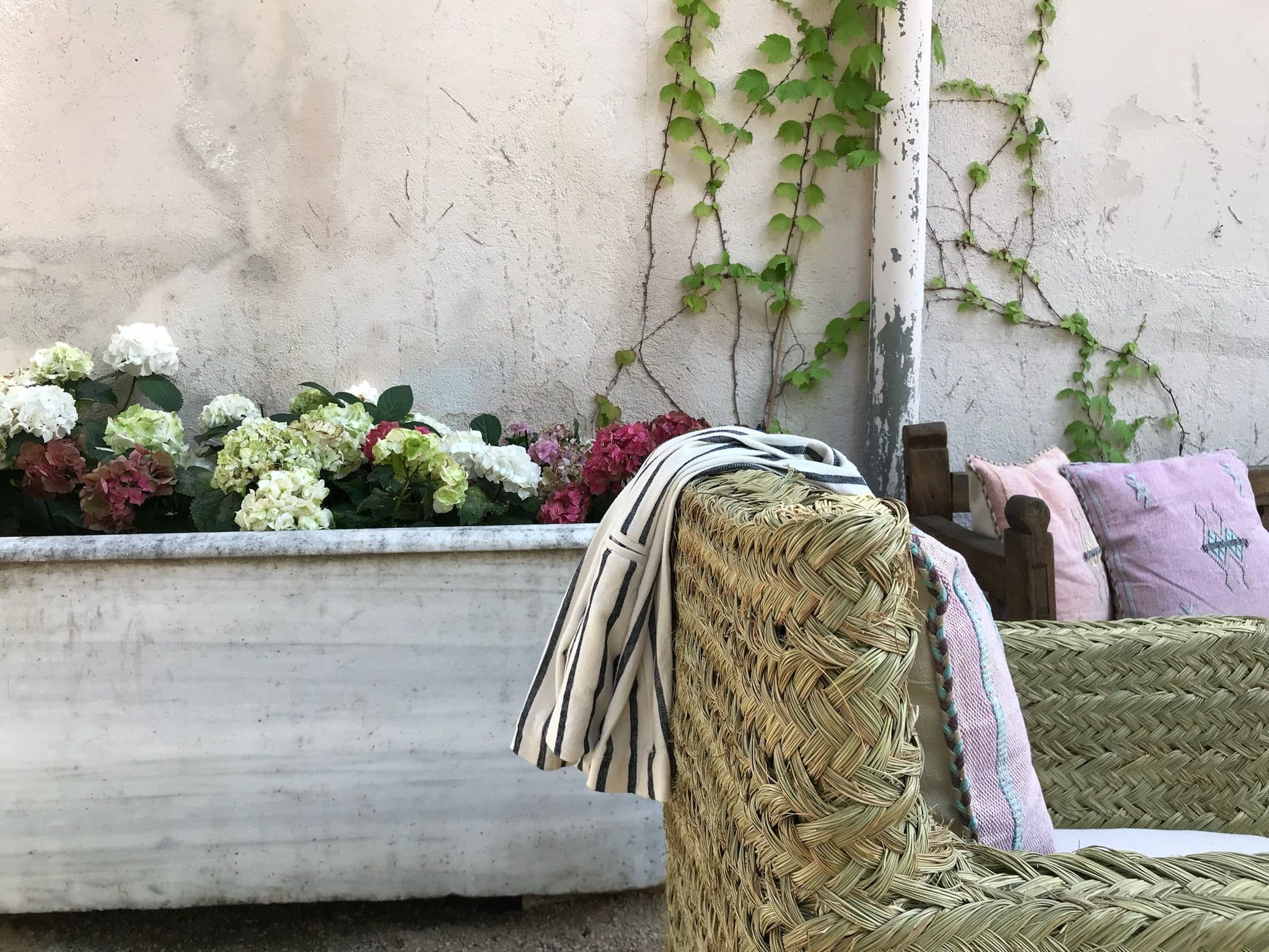 Pila de piedra con hortensias y butaca de fibra vegetal en el jardín