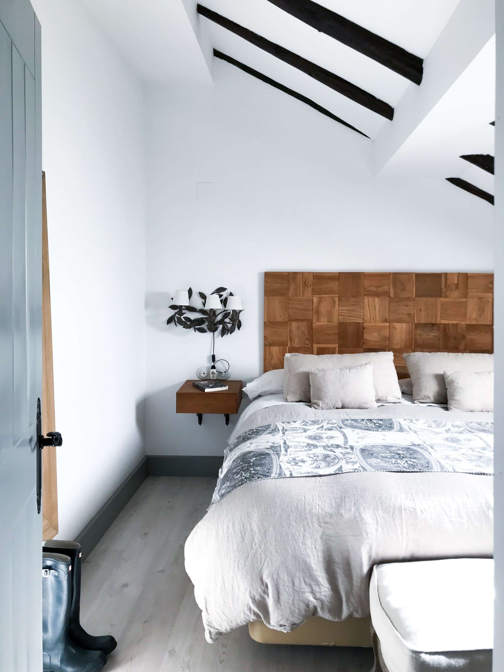Dormitorio con cabecero de tarugos de madera y colcha gris