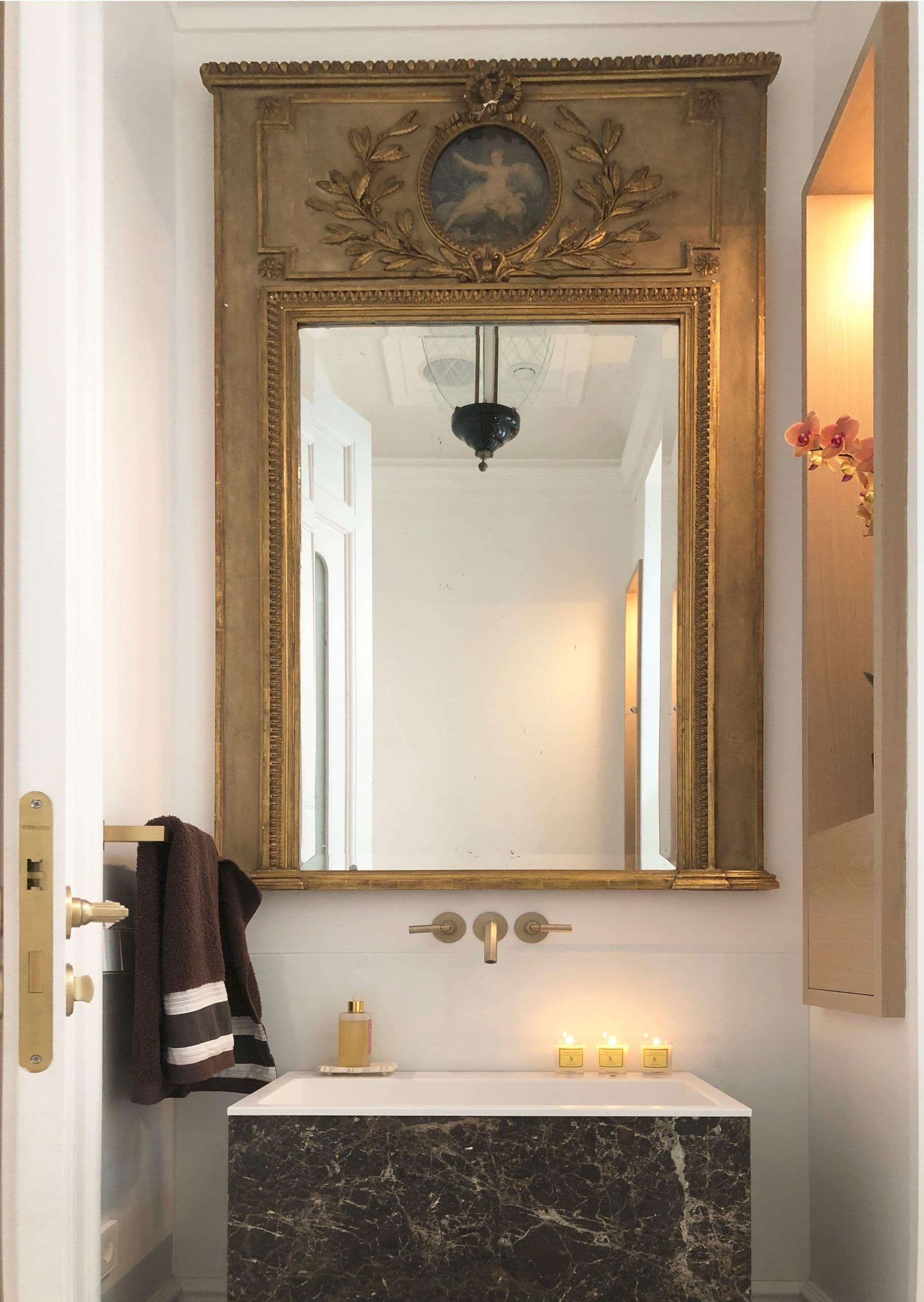 Aseo con espejo dorado de trumeau, lavabo de mármol negro y grifería de pared en latón