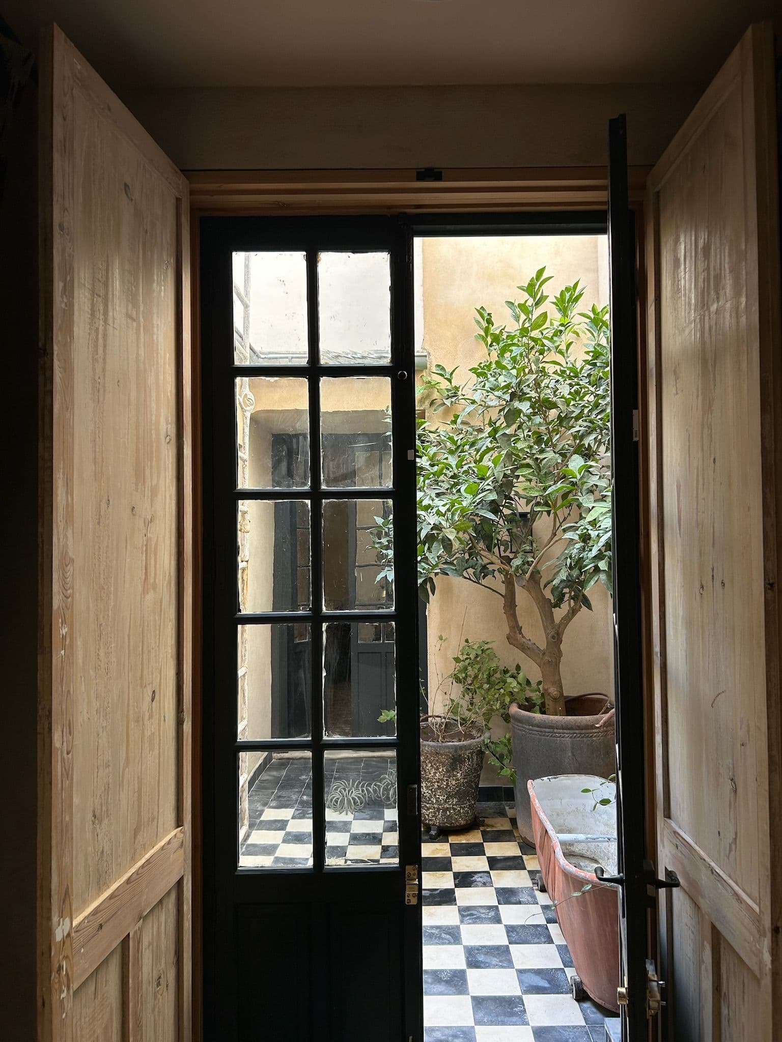 Puertas de pino abiertas al patio, con olivo en maceta y la bañera de cobre al fondo