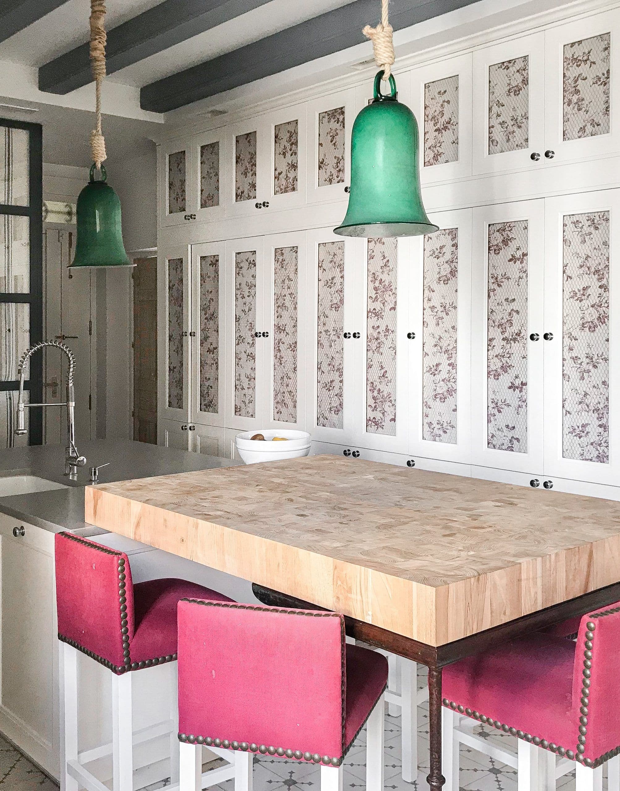 Cocina con isla de tajo de carnicero, campanas de cristal verde y taburetes magenta