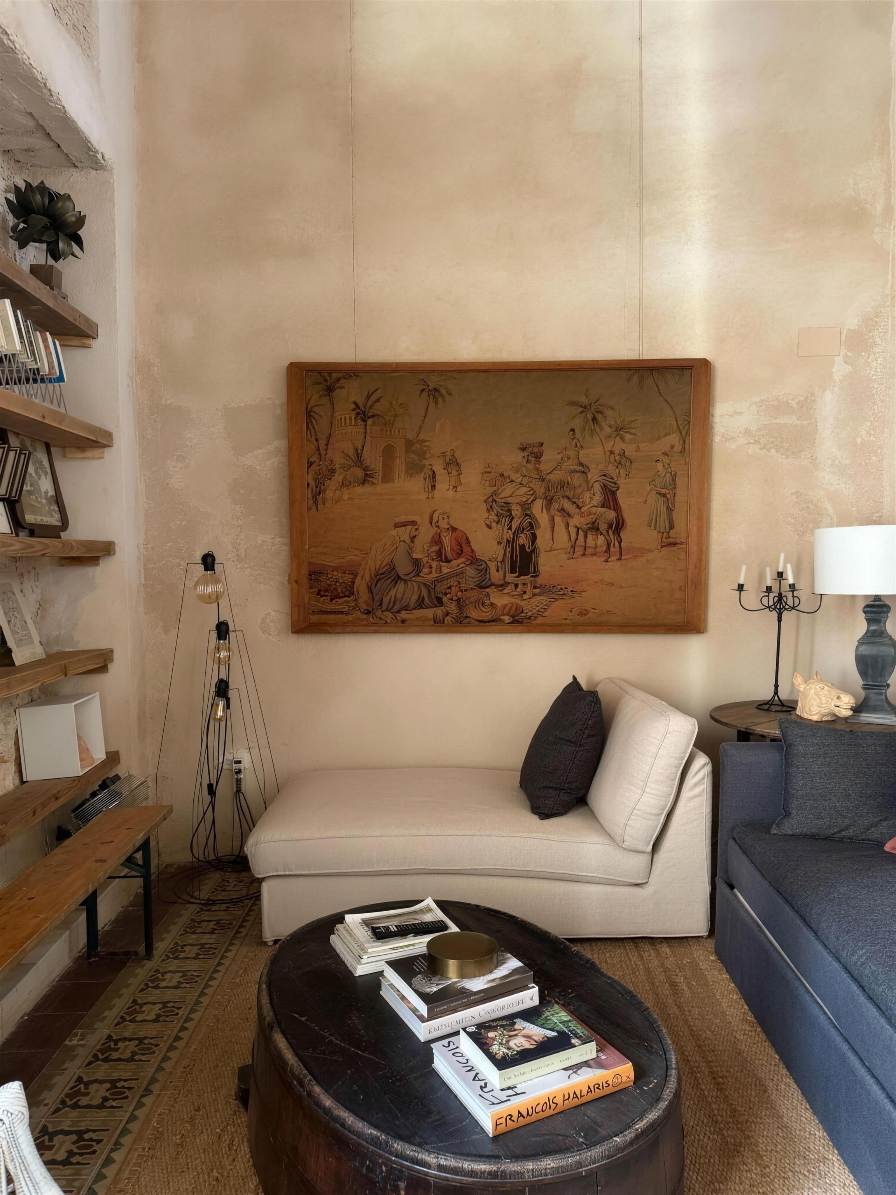 Salón en vertical con tapiz de escena clásica sobre chaise de lino y mesa baúl de cuero