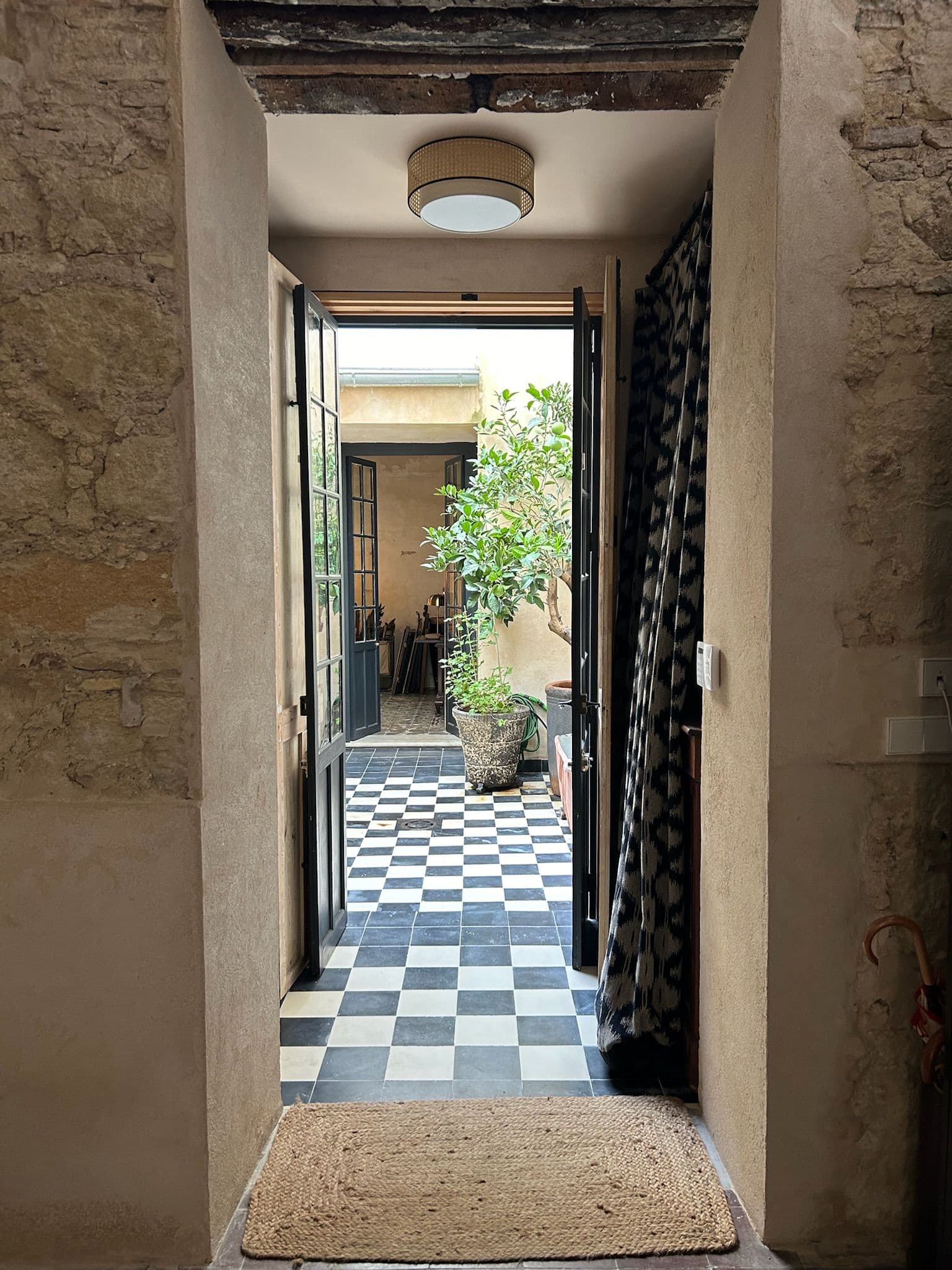 Pasillo de muros de piedra y cal abierto al patio, con suelo ajedrezado y felpudo de esparto