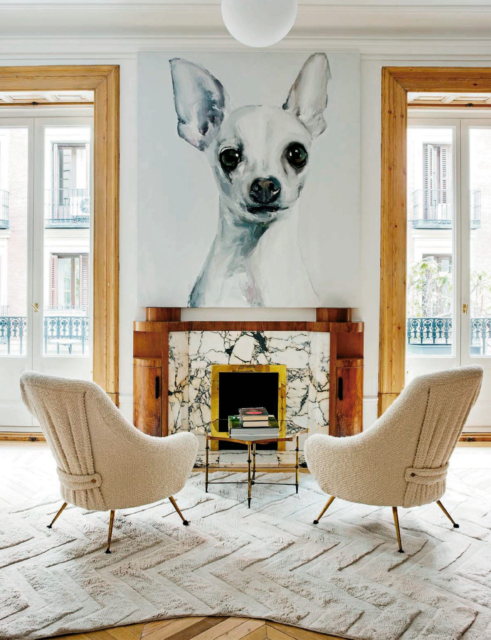 Salón con retrato gigante de un chihuahua sobre chimenea de mármol, flanqueado por dos butacas de bouclé