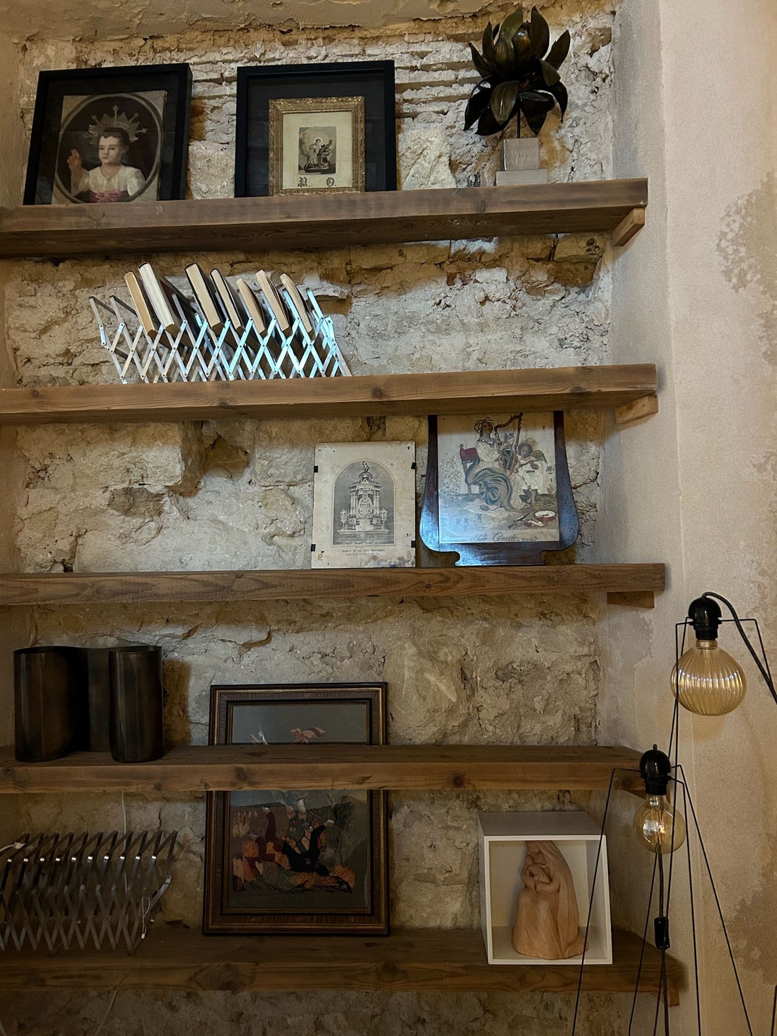 Estanterías de madera recuperada sobre muro de piedra vista, con marcos antiguos y cerámica