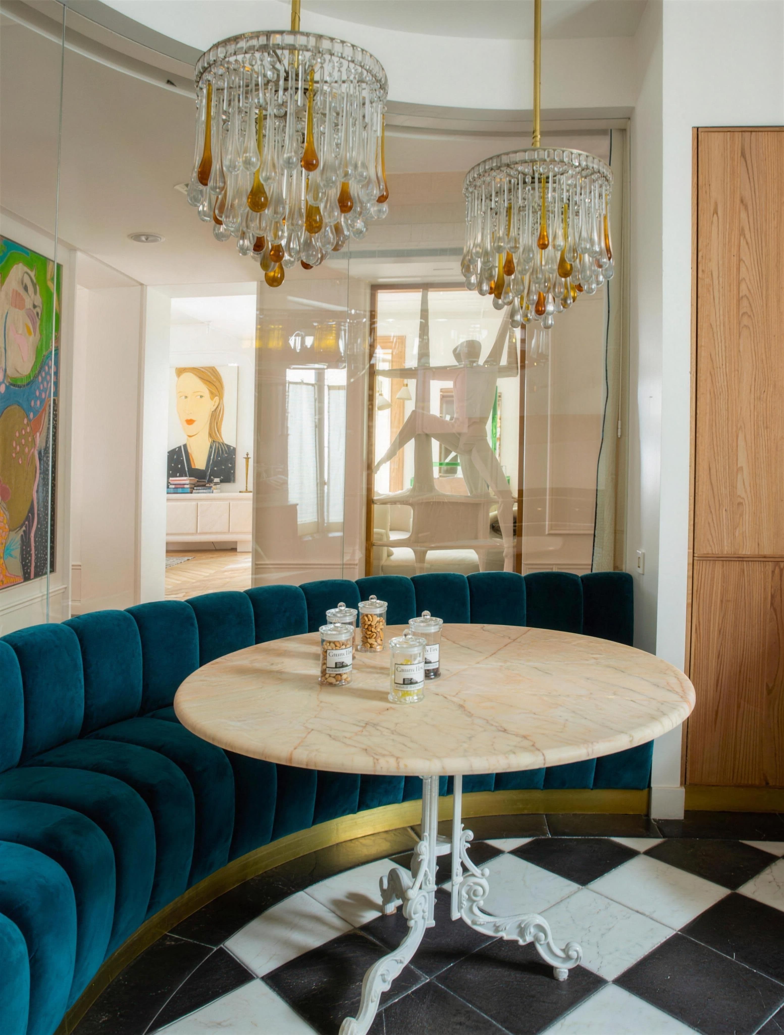 Comedor con banqueta curva de terciopelo azul, mesa de mármol, suelo damero y lámparas de cristal ámbar
