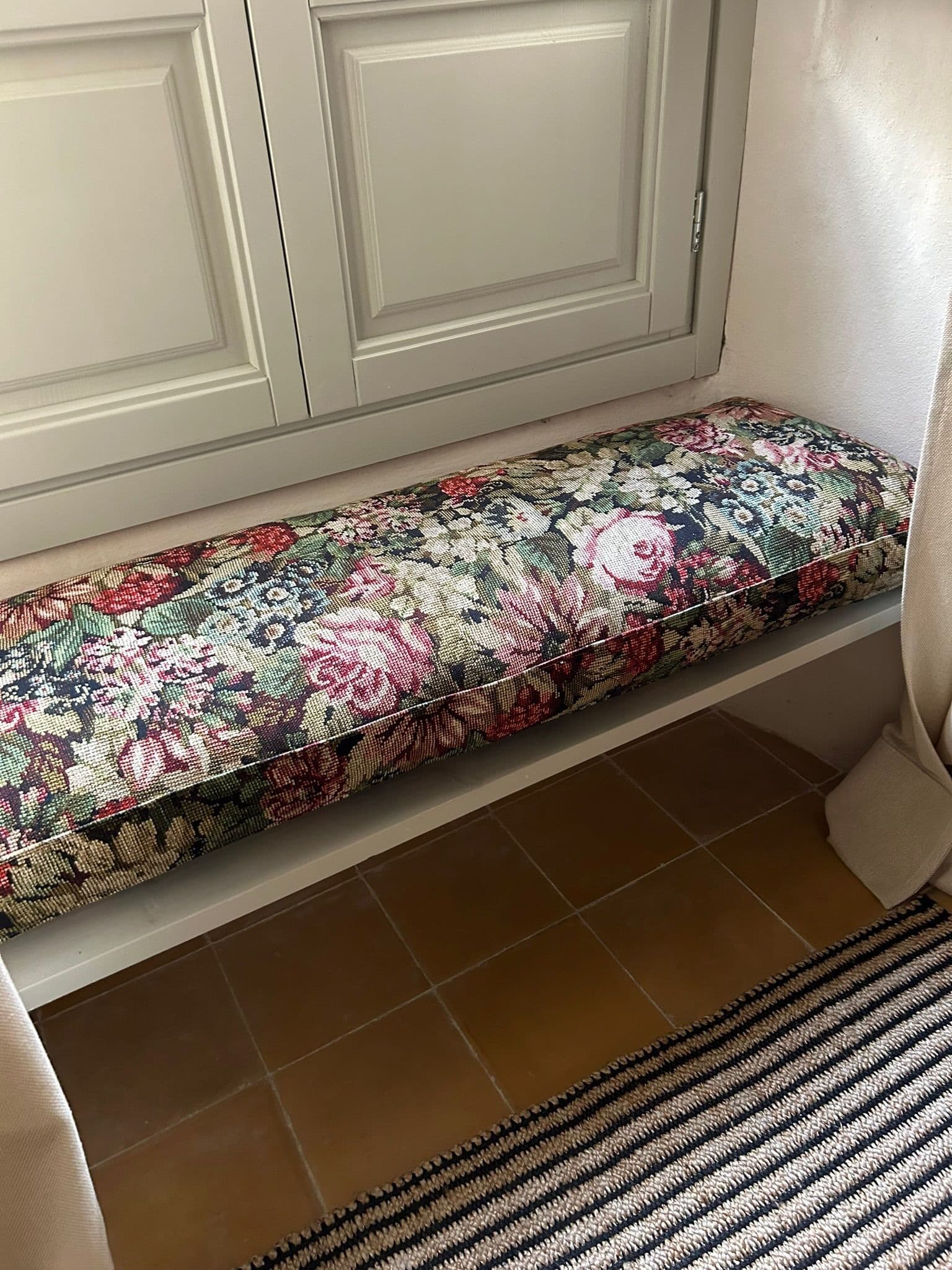 Banco de madera con tapicería floral junto a ventana de contraventanas verdes