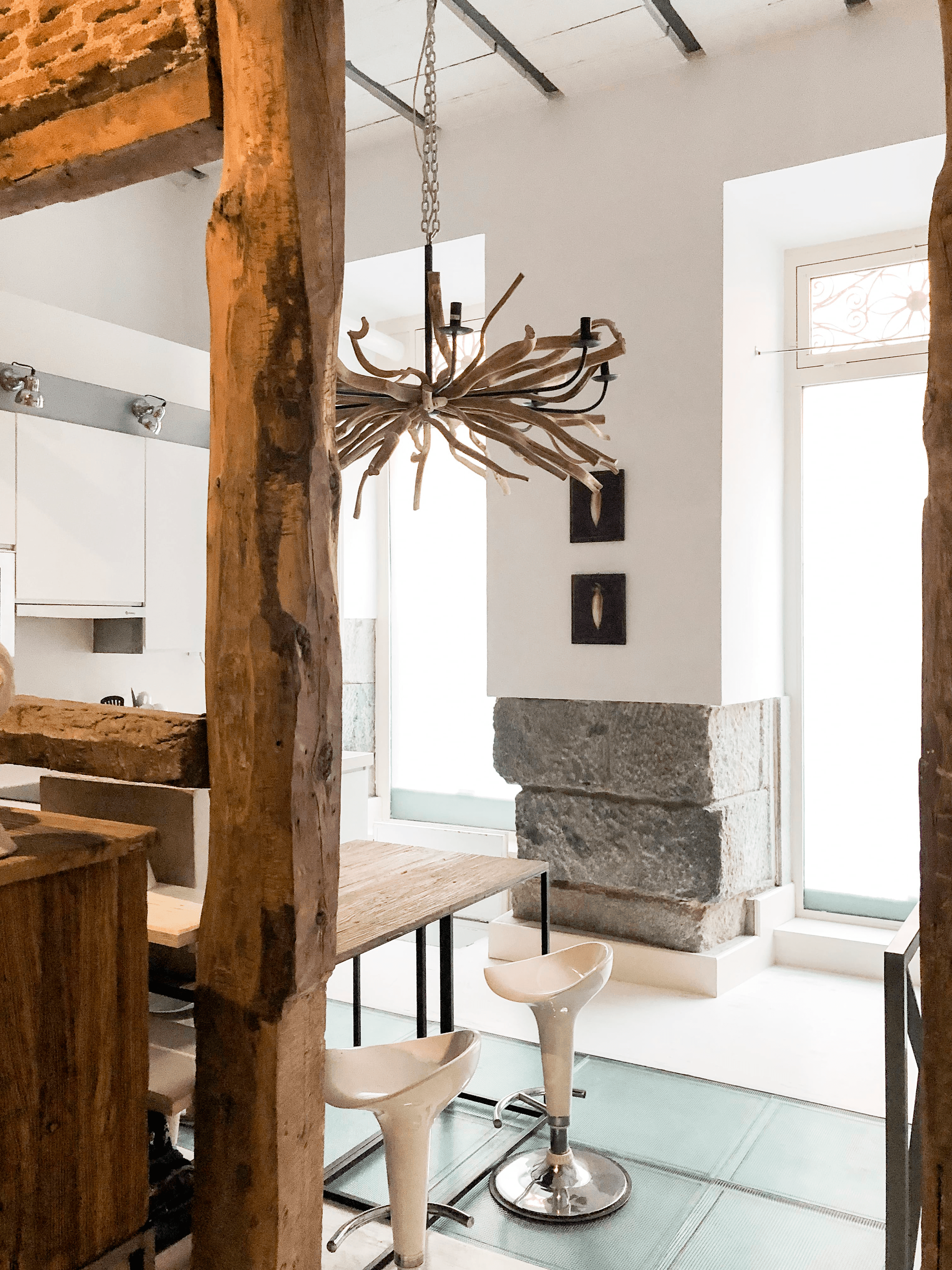 Pie derecho de madera centenaria junto a cocina blanca y taburetes de diseño