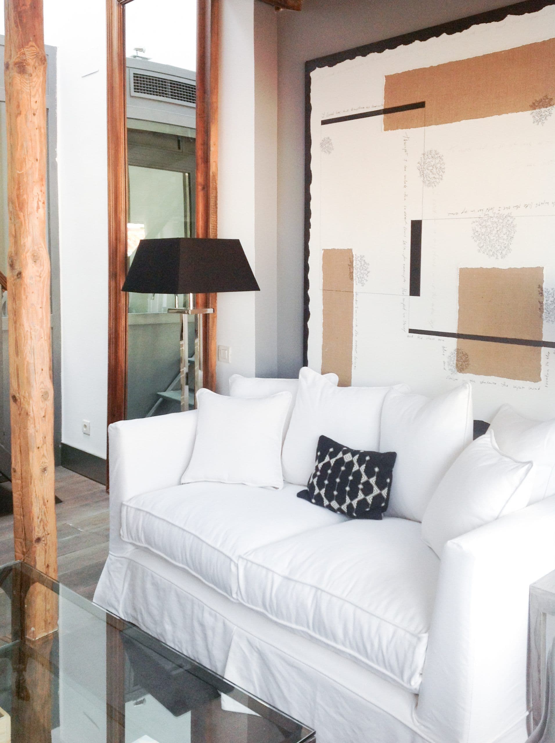Sofá blanco junto a viga de madera vista y galería acristalada