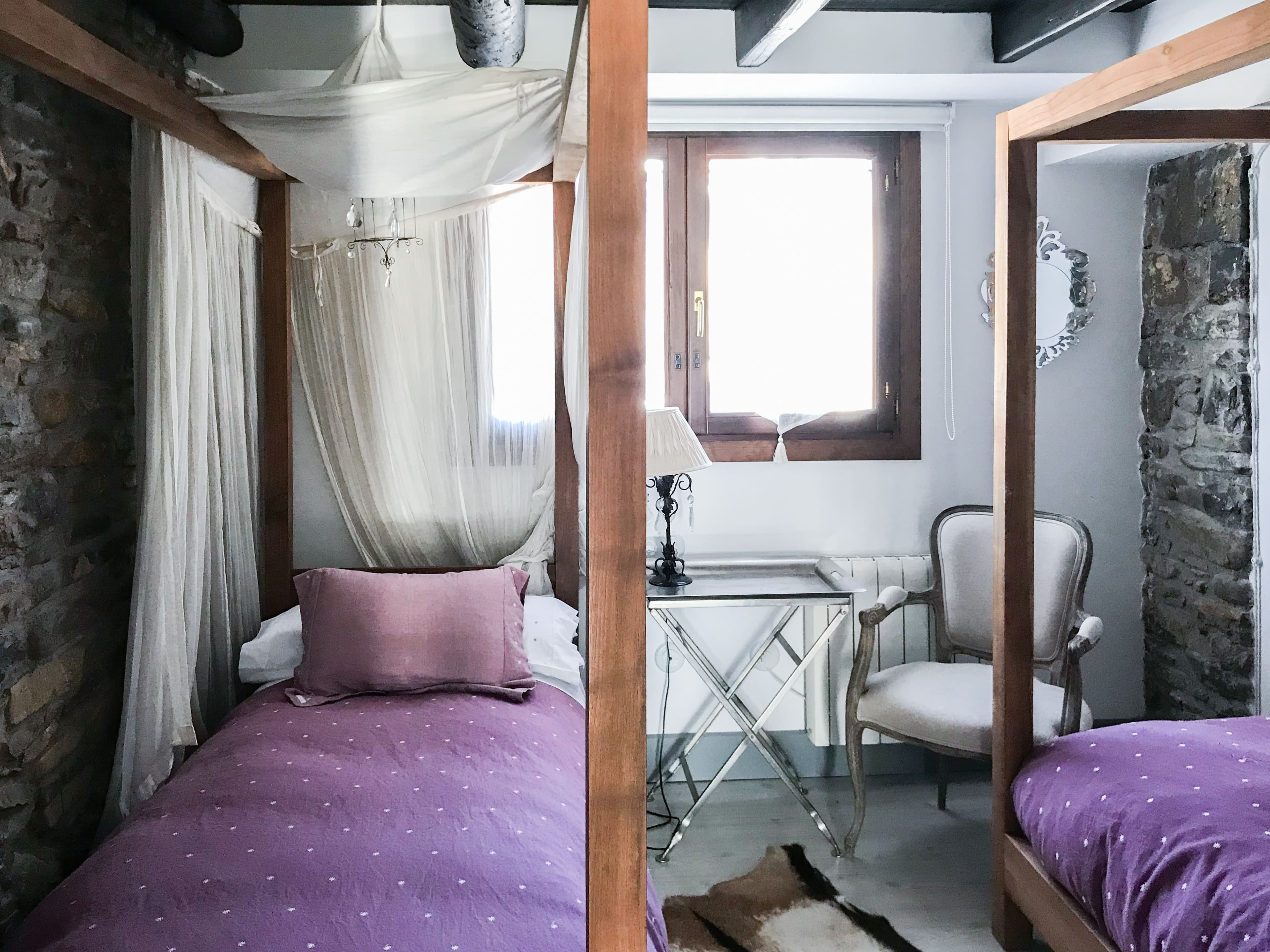Dormitorio con camas con dosel y colchas moradas junto al muro de piedra