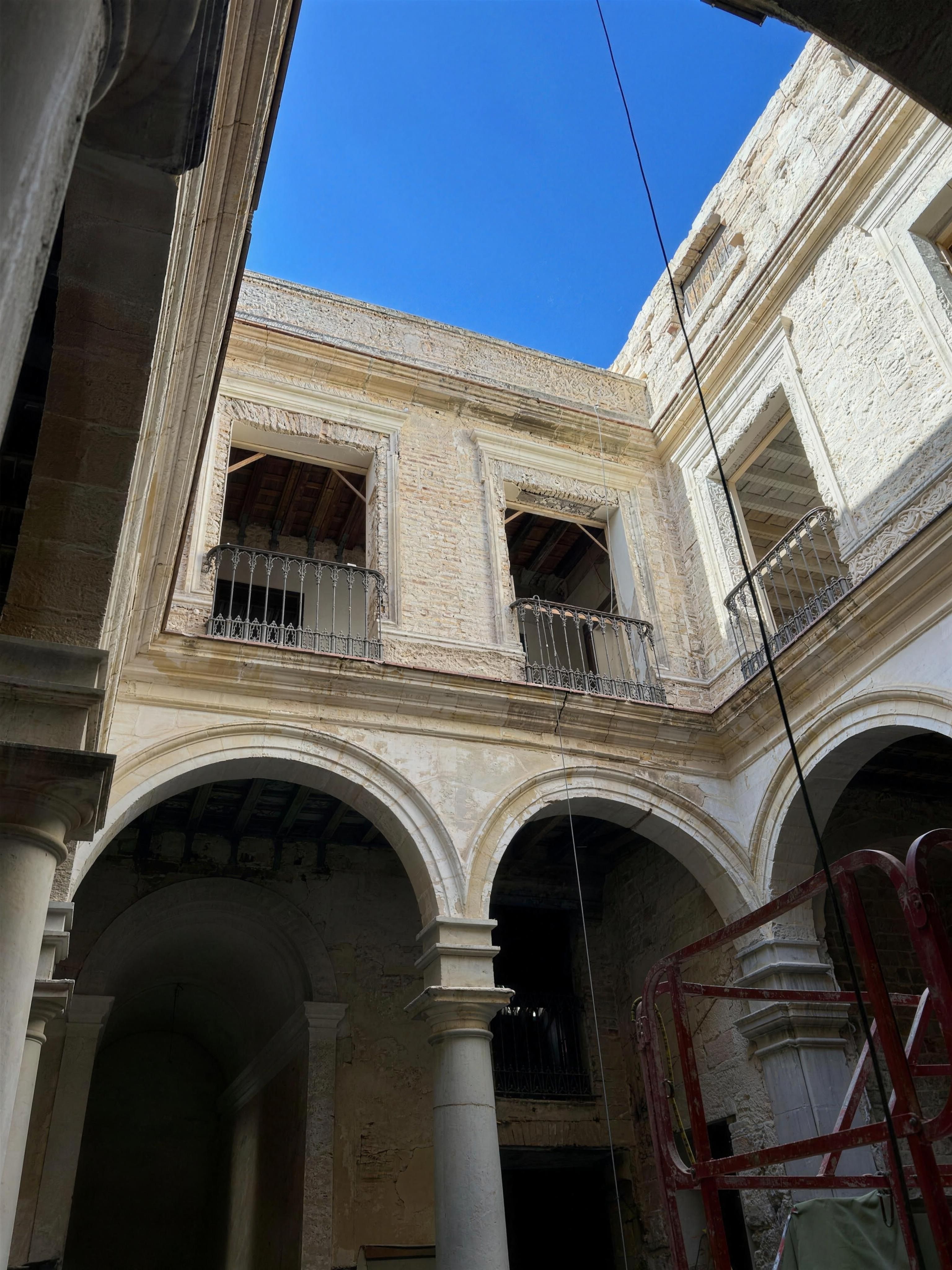 Patio de columnas del palacete en rehabilitación, con arcos de piedra contra el cielo azul