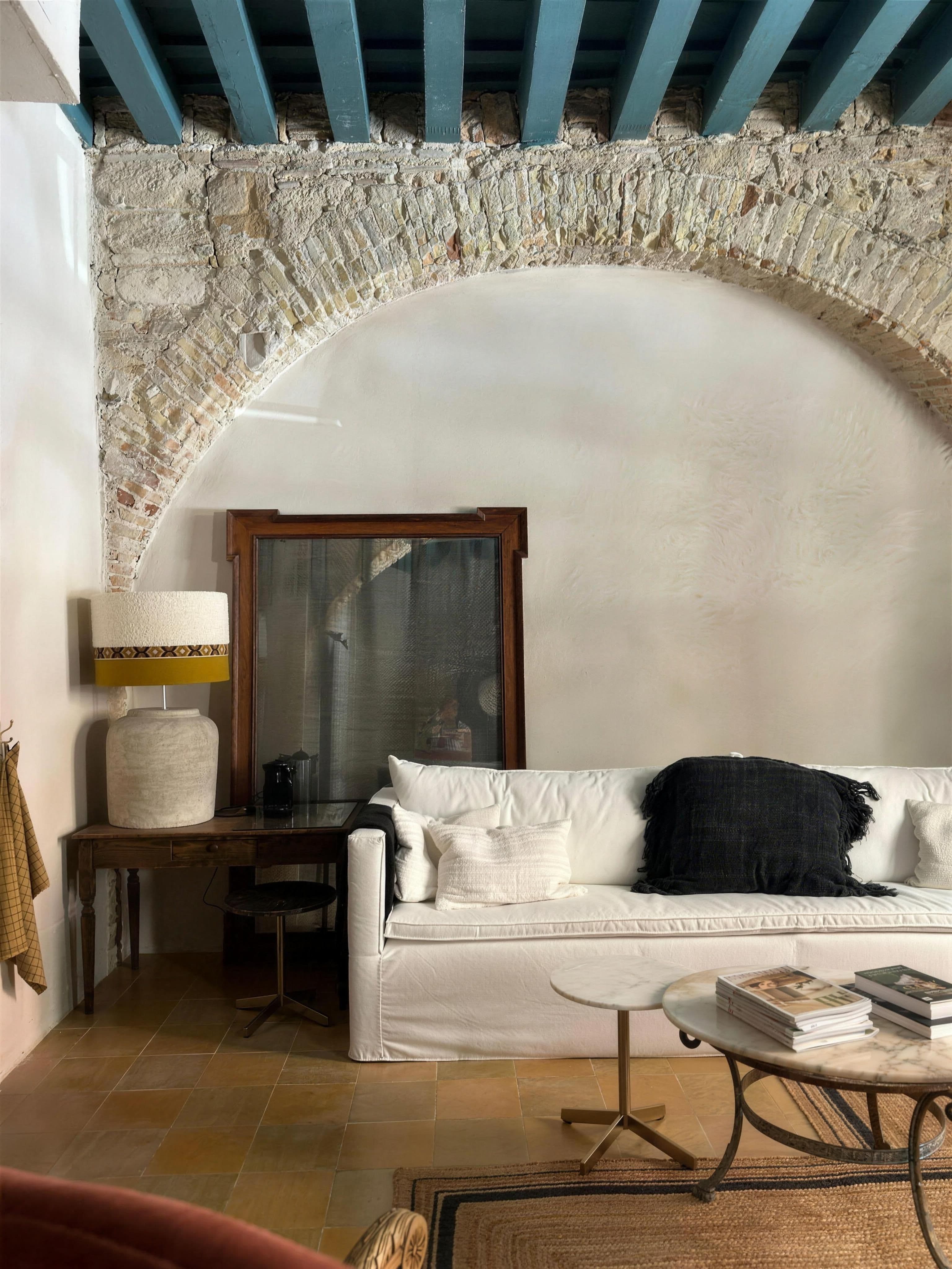 Salón de muro de piedra con arco, sofá blanco y mesa de centro de hierro