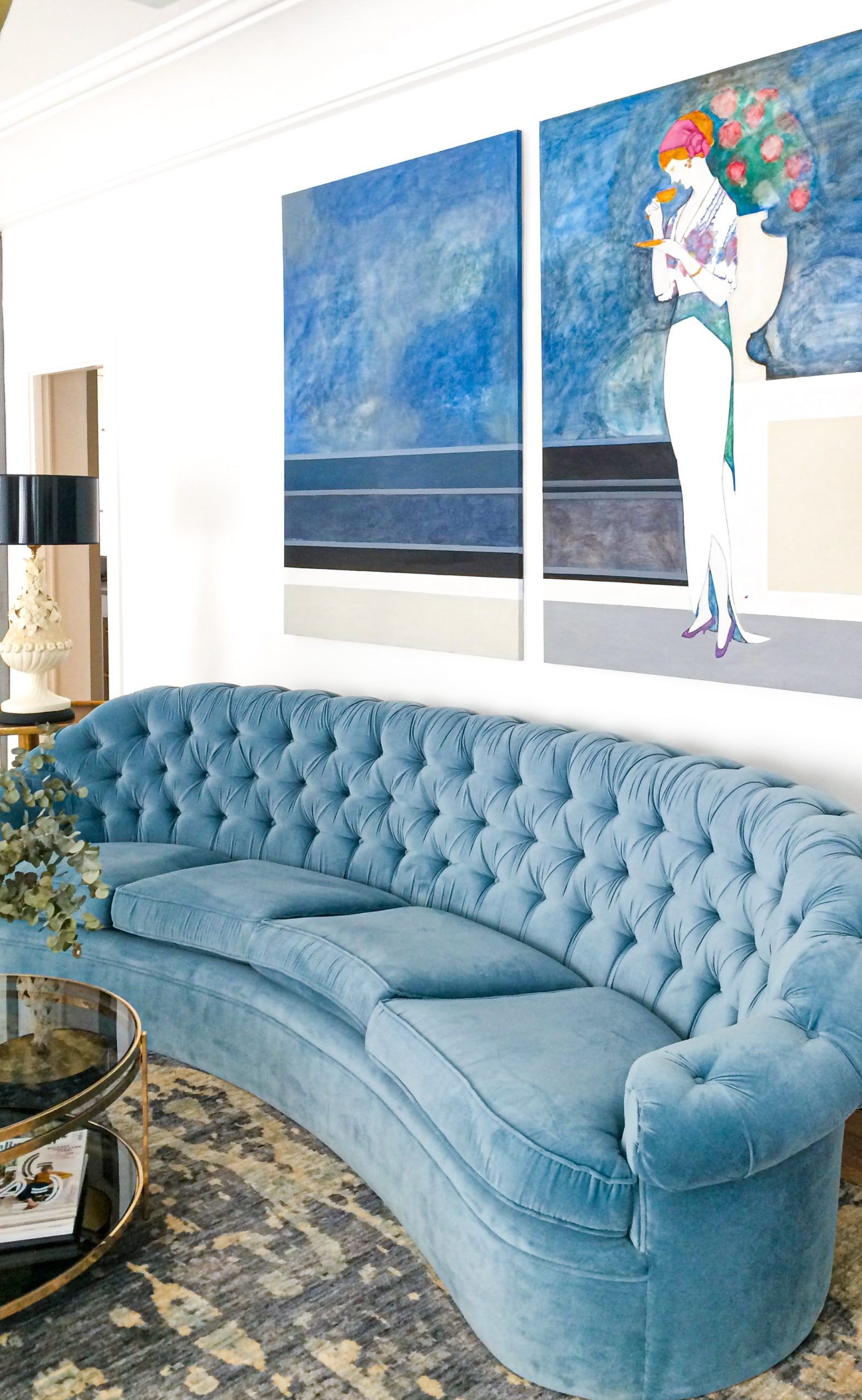 Sofá curvo capitoné de terciopelo azul bajo gran obra figurativa en tonos azules