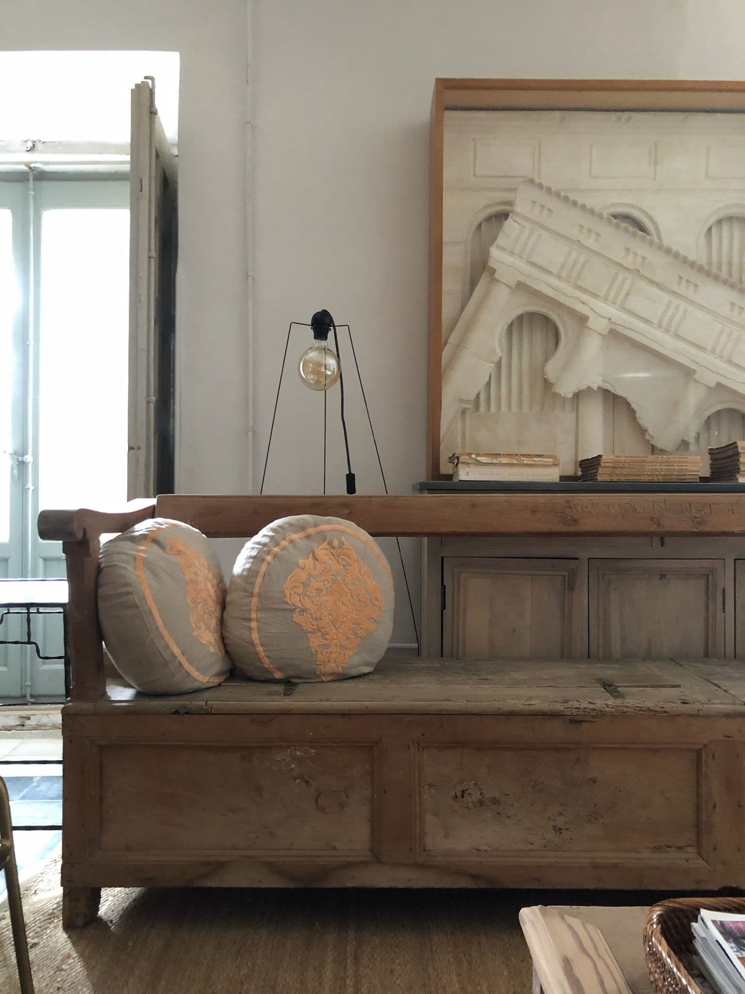 Banco arcón antiguo con cojines bordados y relieve arquitectónico de escayola