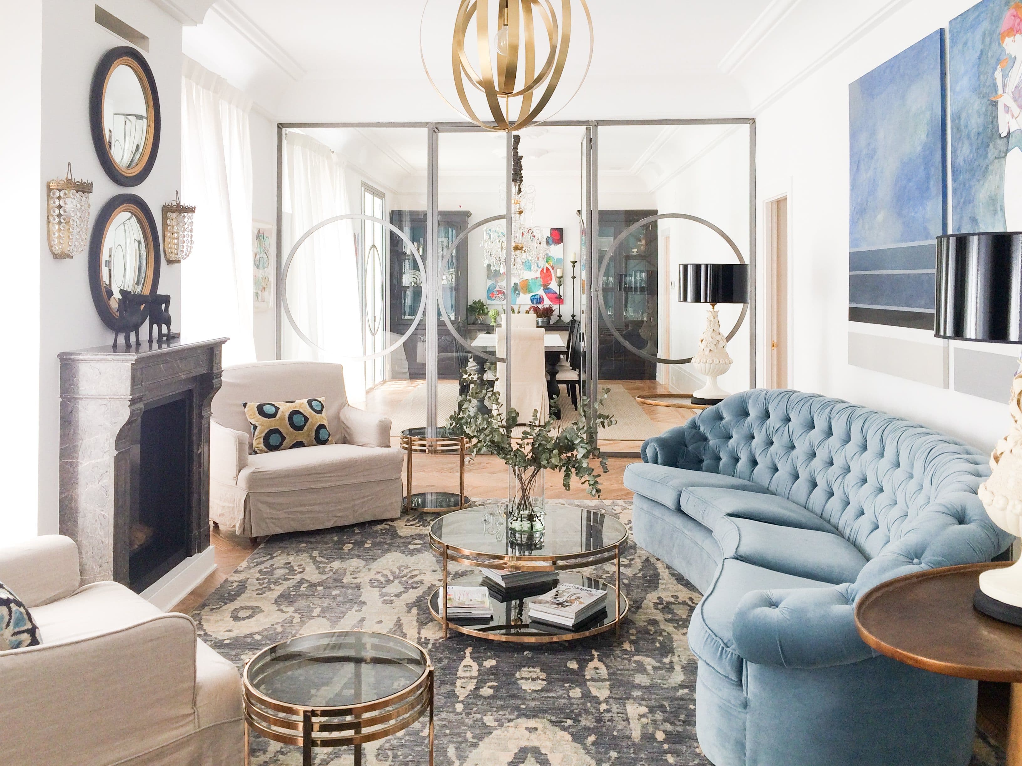 Salón con chesterfield azul, butacas blancas y chimenea enmarcada en espejo