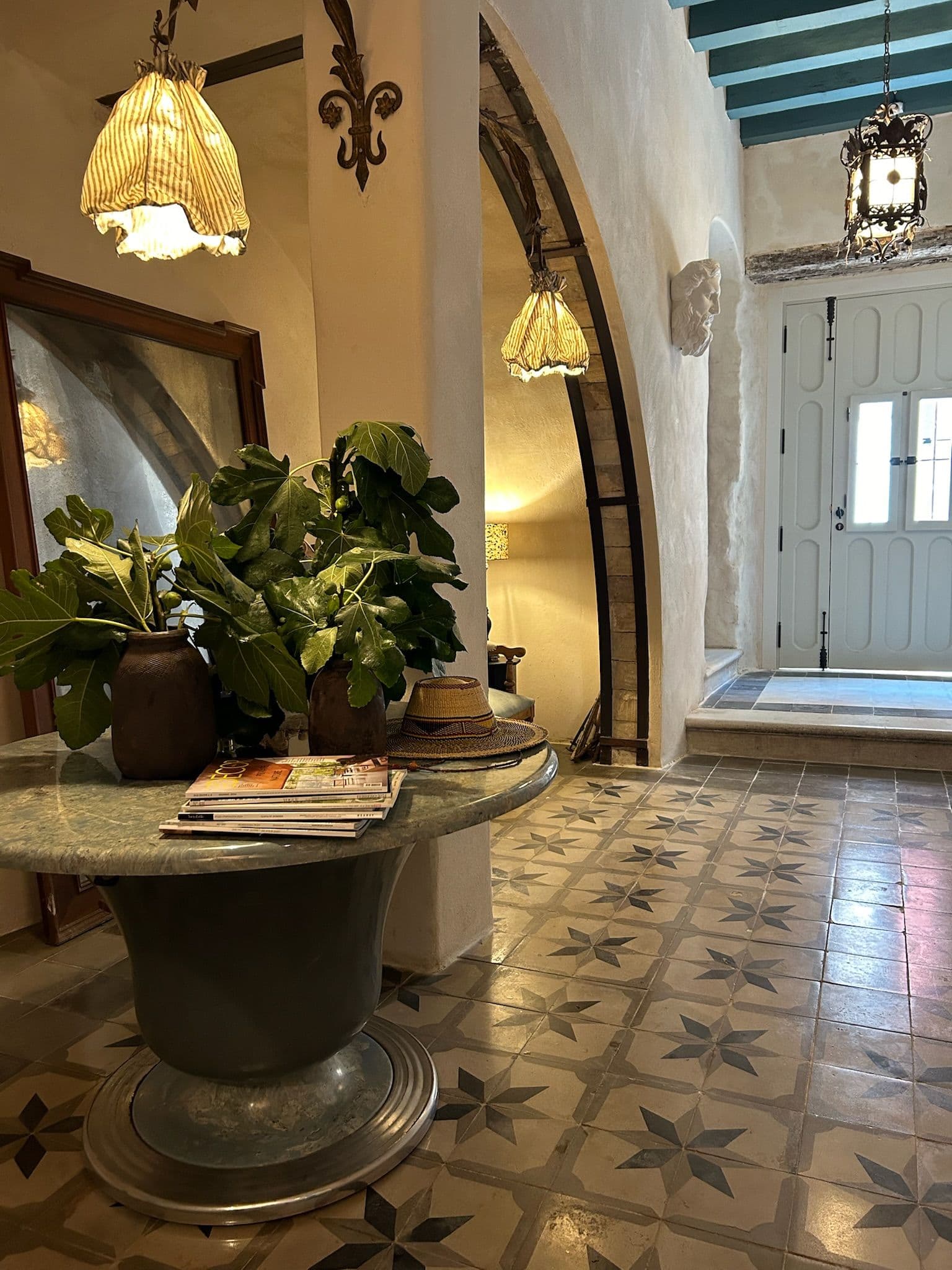 Recibidor con mesa de mármol, helecho y farol bajo arco encalado