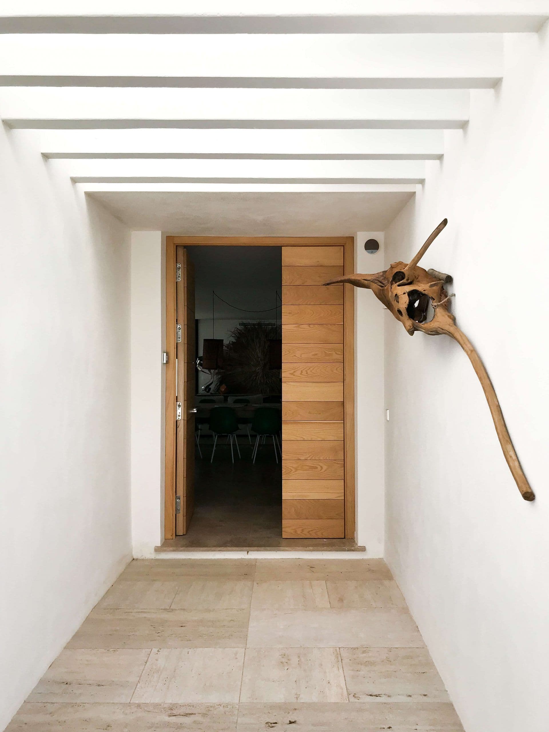Entrada de travertino con puerta de madera y escultura de madera de deriva en el muro